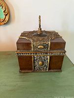 Front view of ornate wood box with metal appliqués and finial