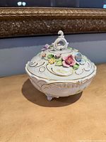 Covered bowl front view showing feet, floral appliqués, gold scrollwork
