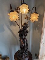 Lamp lit, close view showing figure base and three illuminated frosted floral shades