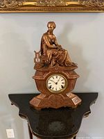 Front view of mantel clock showing figure, dial, base details.