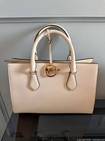 Front view of Michael Kors beige leather satchel showing MK medallion charm and structured silhouette