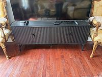 Front view of black fluted-door TV stand under television