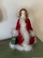 Front view of Royal Doulton Peggy Nisbet Heirloom doll in red coat with white faux fur, holding green bag
