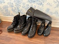 Three pairs of black boots lined up: Dr. Martens lace-up, Michael Kors lace-up, Michael Kors knee-high