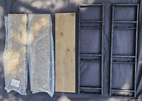 Two metal side frames and three wooden shelves laid out; shelves protected by bubble wrap