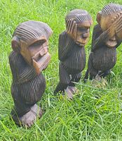 Front angled view of all three carved wooden monkey figurines standing on grass
