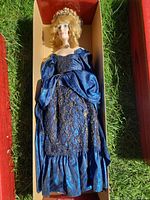 Porcelain doll in blue gown lying in box