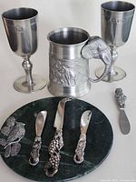 Group shot showing all items: two goblets, elephant tankard, three ornate knives, Santa knife, marble cheese board