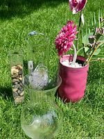 Group view of four decorative pieces: bulbous glass vase, cylindrical glass vase, rectangular glass vase with stones, pink planter with faux flowers