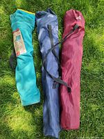 Three camping chairs in teal, navy, maroon bags on grass