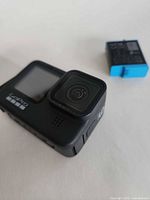 Front view of GoPro HERO9 Black with detached blue-tab battery nearby, showing lens and front screen