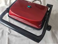 Closed panini press showing red lid, indicator light, handle, cord