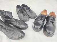 Group shot of three pairs of black men’s footwear: Ecce Home boots, Dr. Martens sneaker-style shoes, Dr. Martens steel-toe shoes