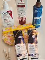 Full lot group shot showing CeraVe lotion, Skinord cream, Bio Active spray, two Clairol boxes, two sample vials and L’Occitane pouch