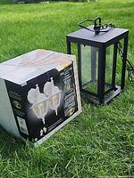 Boxed Hampton Bay twin-pack beside unboxed black pendant light on grass