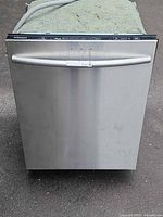 Front view of stainless dishwasher with curved handle and attached drain hose