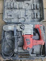 Rotary hammer drill placed inside open molded case, full view of tool, cord, handle and storage case interior