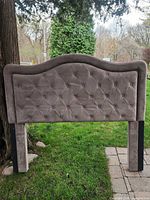 Full front view of grey tufted upholstered queen headboard with wood legs