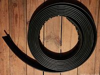 Coiled partial roll of black plastic lawn edging on wood floor