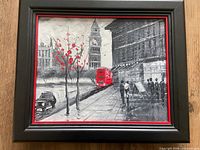 Framed London street scene painting showing Big Ben, red bus, pedestrians, black frame with red trimming