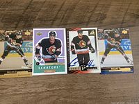 Four Chris Phillips Ottawa Senators trading cards lined on a wooden surface, third card signed in blue ink