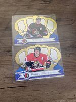 Front view of both die-cut hockey cards in sleeves showing players, gold crown foil design and team logos