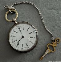 Front view of pocket watch with chain and key showing dial details