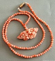 Full view of coral bead necklace coiled with carved floral pendant visible