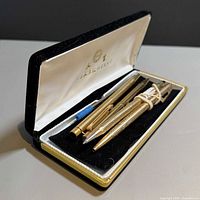 Hinged presentation case open displaying four gold writing instruments and refills