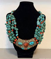 Full view of necklace on bust showing multi-strand turquoise and coral beads with brass pendant