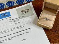 Appraisal document beside ring in box showing diamond solitaire details
