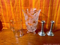 Group view: Mikasa vase, clear glass pitcher, pair pewter candlesticks on wood surface