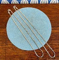 Both silver snake chain necklaces side by side on blue felt