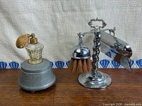 Perfume atomizer on pewter music box base beside chrome crumb catcher set