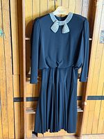 Front view showing full dress, pleated skirt, long sleeves, beaded collar and bow