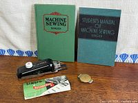 Group shot of buttonholer attachment, two Singer books, instruction booklet, money clip