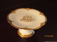 Top view of porcelain pedestal compote showing scalloped rim, gold border, and central monogram