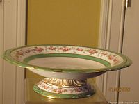 Side profile of porcelain compote showing pedestal base, green and gold trim, floral rim
