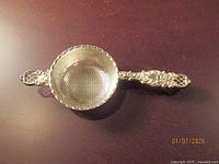 Top view of silver tea strainer showing perforated bowl and ornate handle