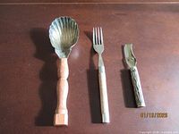 Three utensils laid out: shell spoon, wood-handle fork, lemon peeler