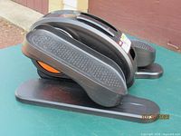 side profile of the compact under-desk elliptical, showing orange flywheel and pedal design