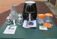 Group shot showing air fryer, drum grater with attachments, manual food processor components and manuals