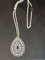 Full view of white enamel filigree pendant on matching chain