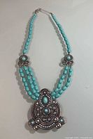 Full view of three-strand faux turquoise bead necklace with large silver-tone pendant