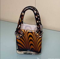 Front view of amber and black tiger swirl glass purse vase with clear twisted handles