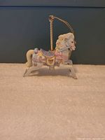 Left side view of porcelain carousel horse ornament showing pastel details and gold pole