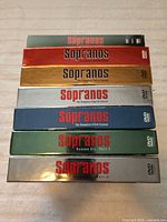 Stacked view of all seven Sopranos DVD box sets showing spine colours and titles