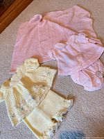 Group shot of yellow knit outfit, pink outfit with bloomers, and pink blanket