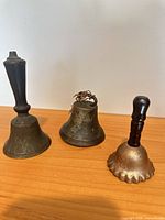 Three metal hand bells on wood surface