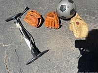Full lot showing three gloves, bike pump, and soccer ball on pavement
